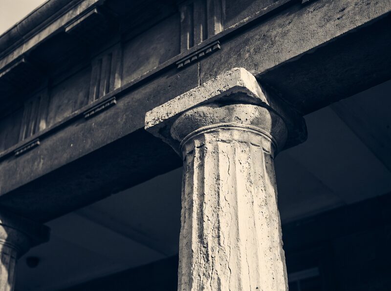Close view of a weathered stone column meeting a shadowed entablature, a neoclassical architectural detail in warm light.